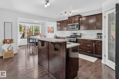 Contemporary kitchen featuring dark wood cabinetry, a central island with an extended breakfast bar, stainless steel appliances, and a white subway tile backsplash - 1115 61 Street Sw, Edmonton, AB - Indoor Photo Showing Kitchen With Upgraded Kitchen