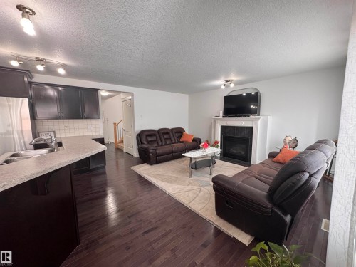 This living space features dark wood flooring, a fireplace with a white mantel, and light-colored walls - 1115 61 Street Sw, Edmonton, AB - Indoor With Fireplace