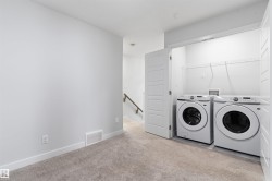 Carpeted room featuring a built-in laundry closet with bi-fold doors, two front-loading machines, and wire shelving - 