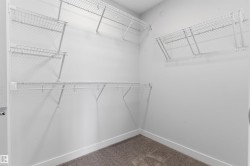 Walk-in closet featuring white wire shelving, multiple hanging rods, and a neutral carpeted floor - 