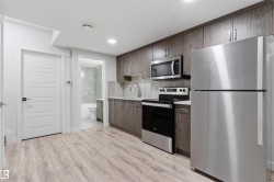 Modern kitchen featuring wood-finish cabinetry, stainless steel appliances including a refrigerator, range, and microwave, and light-toned countertops - 