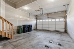 Spacious garage featuring a concrete floor, overhead lighting, an automatic garage door opener, and a wooden staircase - 