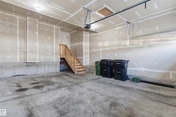 Spacious garage featuring a concrete floor, exposed drywall walls, and a wooden staircase providing interior access - 