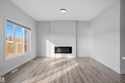 Contemporary living space featuring a built-in linear electric fireplace, large window, overhead flush-mount lighting, light wood-finish flooring, and white baseboards - 