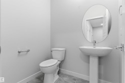 Pedestal sink with chrome faucet, oval mirror, white toilet, and light gray wall paint - 