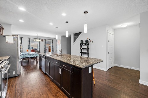 Kitchen island featuring a granite-style countertop, undermount sink, and pendant lighting - 1563 Tamarack Boulevard Nw, Edmonton, AB - Indoor Photo Showing Kitchen With Upgraded Kitchen