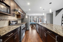 Kitchen featuring dark wood-finish cabinetry, stainless steel appliances, granite countertops, and wood-finish flooring - 