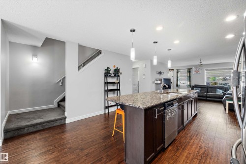 Open-concept main floor featuring wood-finish flooring, a kitchen island with stone countertop, stainless steel dishwasher, and recessed ceiling lighting - 1563 Tamarack Boulevard Nw, Edmonton, AB - Indoor Photo Showing Kitchen With Double Sink With Upgraded Kitchen