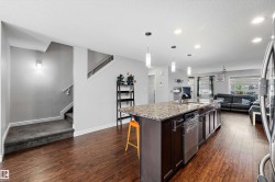 Open-concept main floor featuring wood-finish flooring, a kitchen island with stone countertop, stainless steel dishwasher, and recessed ceiling lighting - 