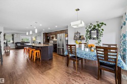 Open-concept living area featuring rich wood-finish flooring, a kitchen island with pendant lighting, dark wood cabinetry, and stainless steel appliances - 