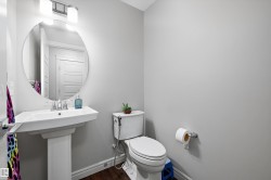 Pedestal sink with chrome fixtures and an oval mirror, complemented by wood-finish flooring, a white toilet, and light gray wall paint - 