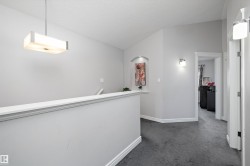 Upper-level landing featuring textured carpeting, white baseboards, a suspended rectangular ceiling light, and a wall niche - 
