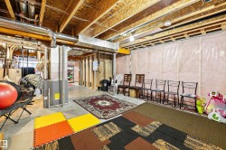 Unfinished basement space featuring exposed wood joists and subfloor, foil-wrapped insulation, and visible utility systems - 