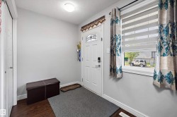 Entryway featuring a white paneled door with decorative glass inserts, wood-finish flooring, a flush-mount ceiling light, and a white-trimmed window with layered shades - 