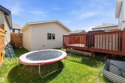 Expansive backyard featuring a wood deck with red-stained railings, a separate structure with vinyl siding and a window, and a wood privacy fence - 