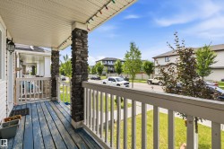Covered front porch featuring stone-clad pillars, white railing, and a blue-painted wood-finish floor - 