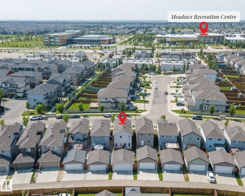 Aerial view showcasing a residential street with attached garages and a community recreation center in the distance - 1563 Tamarack Boulevard Nw, Edmonton, AB - Outdoor With View