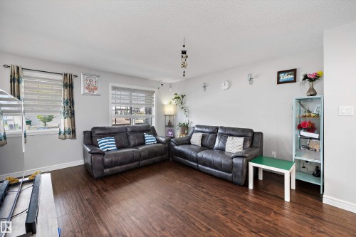 Spacious living area featuring wood-finish flooring, two windows with horizontal blinds, and light gray wall paint - 1563 Tamarack Boulevard Nw, Edmonton, AB - Indoor Photo Showing Living Room