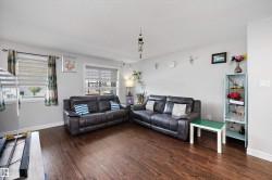 Spacious living area featuring wood-finish flooring, two windows with horizontal blinds, and light gray wall paint - 