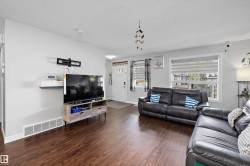 Spacious living area featuring wood-finish flooring, light gray walls, and large windows with blinds - 