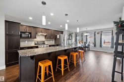Open-concept kitchen featuring dark wood cabinetry, stainless steel appliances, granite countertops, and a large island with pendant lighting - 