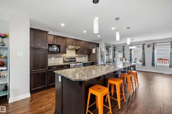Open-concept kitchen featuring wood-finish flooring, dark wood cabinetry, granite countertops, a tiled backsplash, and stainless steel appliances - 