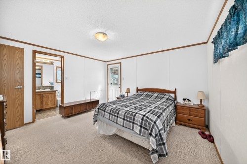Spacious bedroom featuring neutral carpeting, a ceiling-mounted light fixture, and a white paneled wall finish with wood trim - #225 3400 48 St, Stony Plain, AB - Indoor Photo Showing Bedroom
