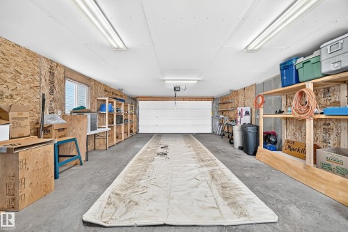 Spacious garage featuring a concrete floor, built-in shelving, white overhead door, and fluorescent lighting - #225 3400 48 St, Stony Plain, AB - Indoor Photo Showing Garage