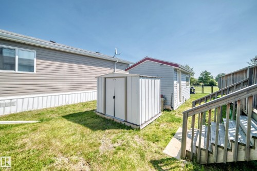 Side yard featuring a metal storage shed, wood exterior stairs with railings, and a fenced-in grassy area - #225 3400 48 St, Stony Plain, AB - Outdoor With Exterior