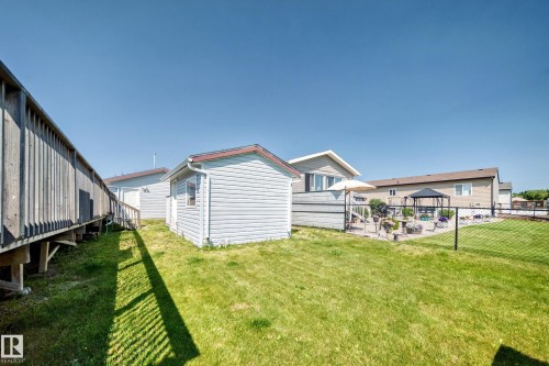 Spacious backyard featuring a manicured lawn, a detached storage shed, a black chain-link fence, a paved patio area, and a privacy fence - #225 3400 48 St, Stony Plain, AB - Outdoor With Exterior