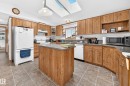 Open kitchen featuring extensive wood-finish cabinetry, a central island with a solid surface countertop, tile flooring, and integrated skylights - #225 3400 48 St, Stony Plain, AB  - Indoor Photo Showing Kitchen With Double Sink 