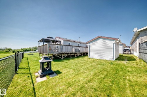 Expansive backyard featuring a manicured lawn, chain-link fencing, a raised wood deck, and an outdoor storage shed - #225 3400 48 St, Stony Plain, AB - Outdoor With Deck Patio Veranda With Exterior