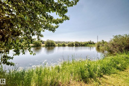 Expansive water feature bordered by lush green foliage and mature trees, under a bright, clear sky - #225 3400 48 St, Stony Plain, AB - Outdoor With Body Of Water With View