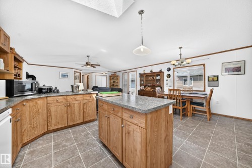 Open-concept kitchen and dining area featuring wood-finish cabinetry, a central island with a solid surface countertop, tiled flooring, and a skylight - #225 3400 48 St, Stony Plain, AB - Indoor Photo Showing Kitchen