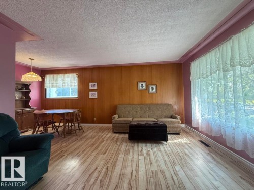 Spacious living area featuring wood-finish flooring, wood paneling, and a large window - 9908 96A Avenue, Fort Saskatchewan, AB - Indoor Photo Showing Living Room