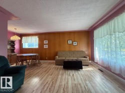 Spacious living area featuring wood-finish flooring, wood paneling, and a large window - 