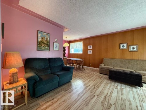 Spacious interior featuring wood-finish flooring, a full wood paneled wall, and a dining area with window - 9908 96A Avenue, Fort Saskatchewan, AB - Indoor Photo Showing Living Room