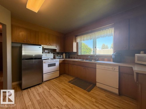 Kitchen featuring wood-finish cabinetry, light countertops, wood-finish flooring, and a stainless steel refrigerator - 9908 96A Avenue, Fort Saskatchewan, AB - Indoor Photo Showing Kitchen With Double Sink