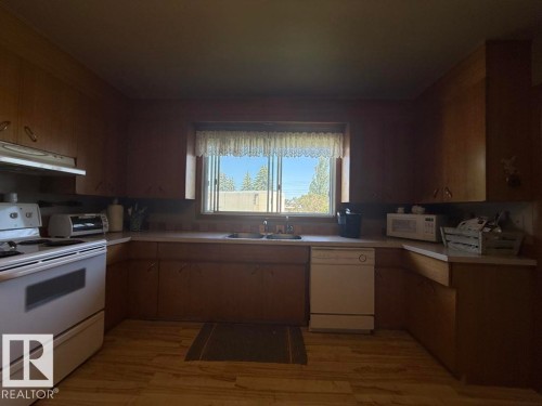 Kitchen featuring wood-finish cabinetry, white countertops, and a double basin sink beneath a window - 9908 96A Avenue, Fort Saskatchewan, AB - Indoor Photo Showing Kitchen With Double Sink