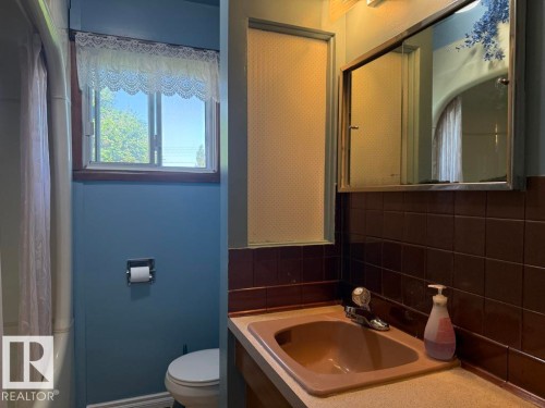 Bathroom featuring a window with natural light, a built-in medicine cabinet, a vanity with an integrated sink, and brown tiled walls - 9908 96A Avenue, Fort Saskatchewan, AB - Indoor Photo Showing Bathroom