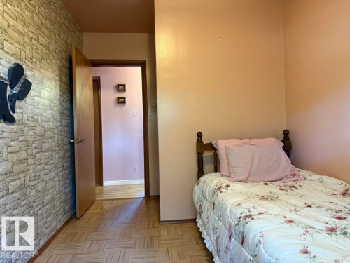 Parquet wood-finish flooring extending into the hallway, a feature wall with stone-look wallpaper, and a solid wood door frame - 9908 96A Avenue, Fort Saskatchewan, AB - Indoor Photo Showing Bedroom