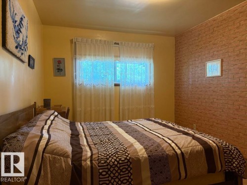 Interior room featuring a window with sheer curtains, a light-colored ceiling, and a brick-patterned accent wall - 9908 96A Avenue, Fort Saskatchewan, AB - Indoor Photo Showing Bedroom