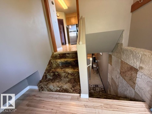 Split-level entryway featuring wood-finish flooring, a carpeted staircase with a decorative pattern, and a stone-look accent wall - 9908 96A Avenue, Fort Saskatchewan, AB - Indoor Photo Showing Other Room