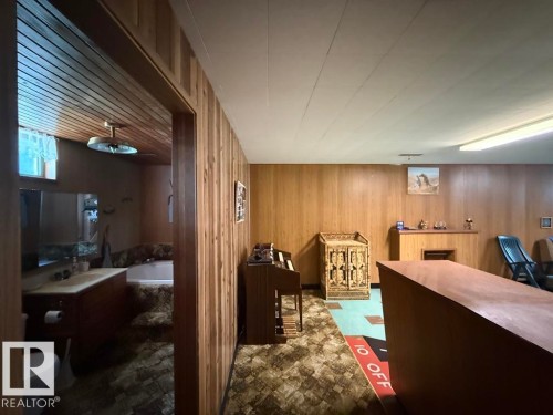 Wood paneling throughout this versatile space, featuring a built-in counter with an integrated fireplace opening and overhead lighting - 9908 96A Avenue, Fort Saskatchewan, AB - Indoor