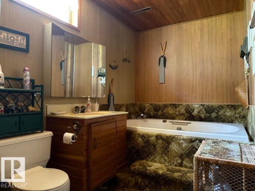 Bathroom featuring a built-in tub, a single vanity with a laminate countertop, a medicine cabinet, a toilet, and wood-finish paneling - 9908 96A Avenue, Fort Saskatchewan, AB - Indoor Photo Showing Bathroom