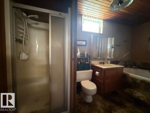 Bathroom featuring a shower stall with sliding glass doors, a vanity with wood-finish cabinetry, a white toilet, and a bathtub with a stone-look surround - 9908 96A Avenue, Fort Saskatchewan, AB - Indoor Photo Showing Bathroom