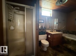 Bathroom featuring a shower stall with sliding glass doors, a vanity with wood-finish cabinetry, a white toilet, and a bathtub with a stone-look surround - 