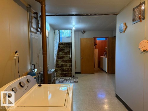 Utility area featuring light-toned flooring, exposed copper piping, and a visible staircase with patterned carpeting - 9908 96A Avenue, Fort Saskatchewan, AB - Indoor Photo Showing Laundry Room