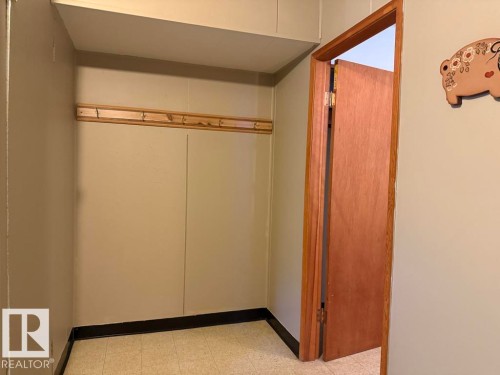 Recessed wall area featuring a wood-finish coat rack with hooks, light neutral wall paint, and dark baseboards - 9908 96A Avenue, Fort Saskatchewan, AB - Indoor Photo Showing Other Room
