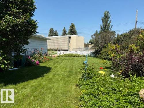 Expansive lawn area featuring a picket fence, mature landscaping, and vibrant flower beds - 9908 96A Avenue, Fort Saskatchewan, AB - Outdoor